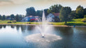 Fountain in a lake with houses and trees in the background