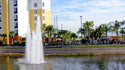 Fountain in a pond with apartment buildings and palm trees in the background