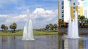 Fountains in a pond with a building and palm trees in the background
